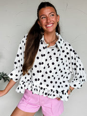 Woman wearing a white blouse with black polka dots and pink shorts against a light background