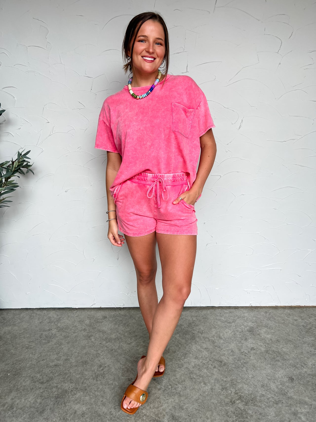 Woman wearing a pink outfit standing against a white wall.