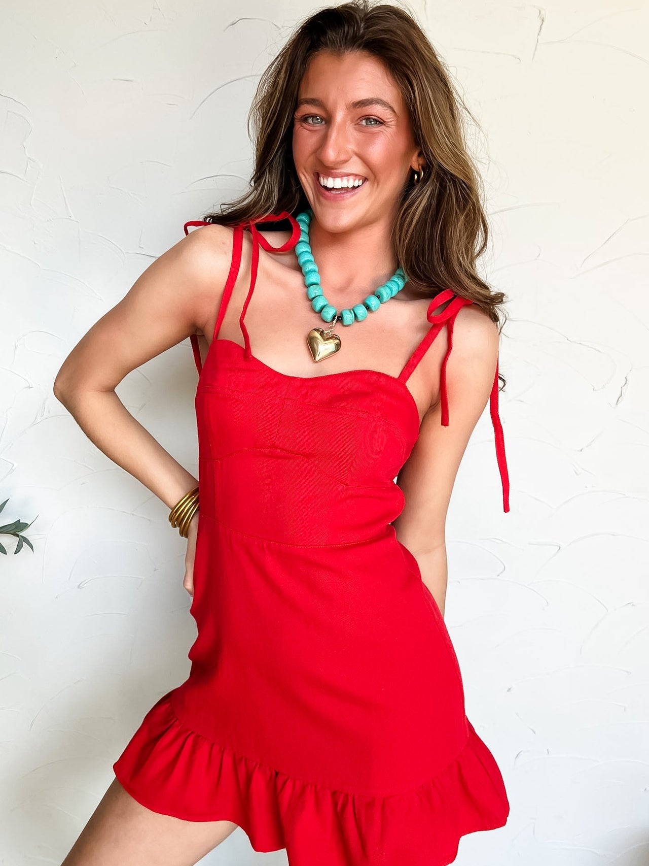 Woman wearing a red dress with bow straps and standing against a white wall.