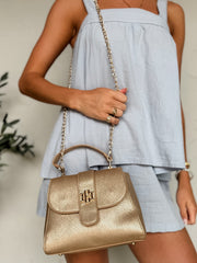 Woman holding a gold handbag with a light blue dress against a neutral background