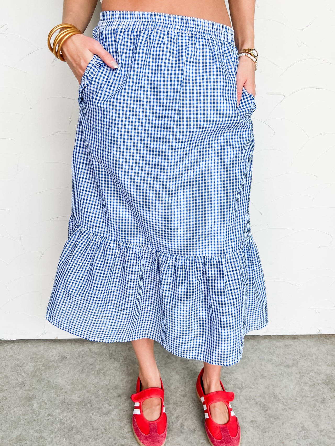 Person wearing a blue checkered midi skirt with red sandals on a plain background