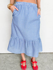 Person wearing a blue checkered midi skirt with red sandals on a plain background