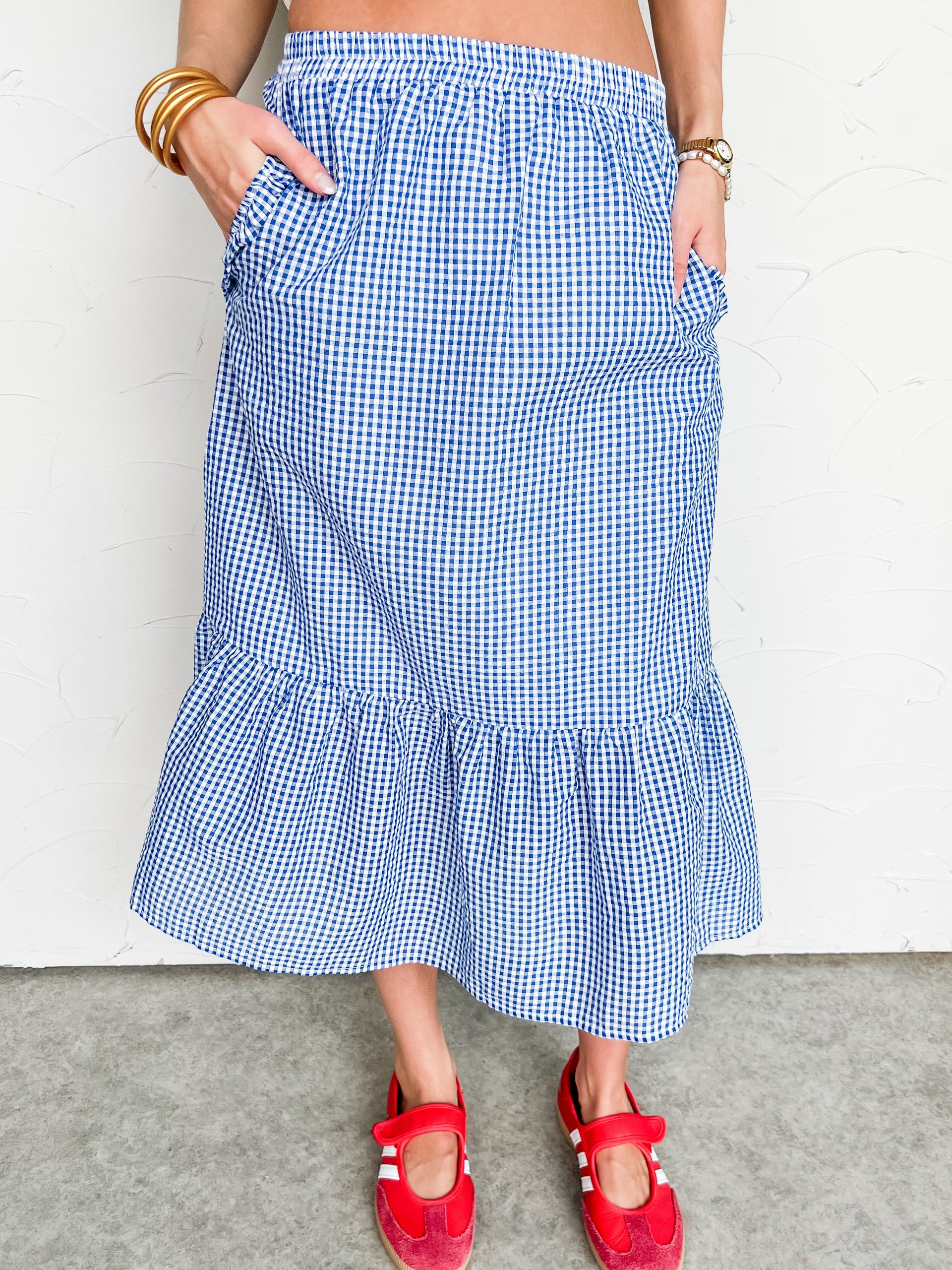 Person wearing a blue checkered midi skirt with red sandals on a plain background