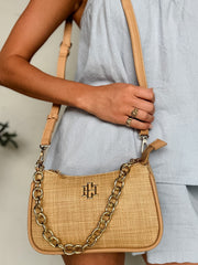 Person holding a beige handbag with a chain detail, wearing a light blue dress.