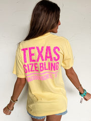 Woman wearing a yellow t-shirt with pink text on the back, standing against a white wall.