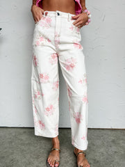 White jeans with pink floral pattern worn by a person against a gray background