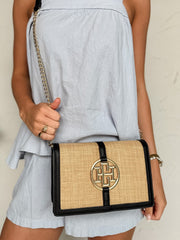 Woman holding a black and beige handbag with a gold clasp against a neutral background