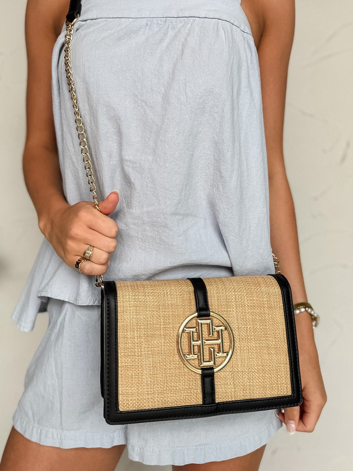 Woman holding a black and beige handbag with a gold clasp against a neutral background