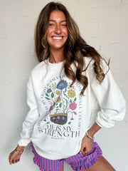 Woman wearing a white sweatshirt with floral design and text, standing against a light background