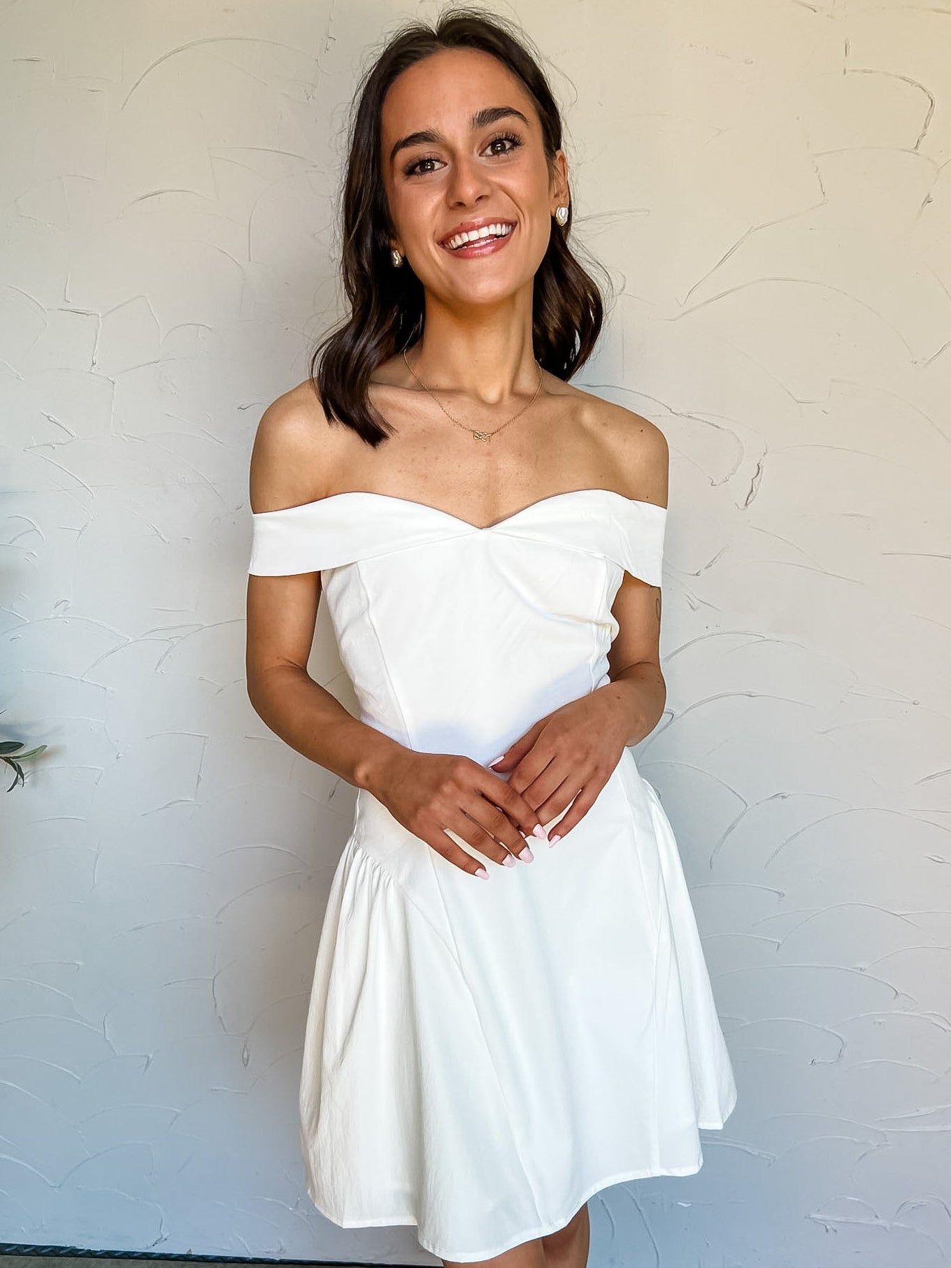 Woman wearing a white off-shoulder dress against a plain background