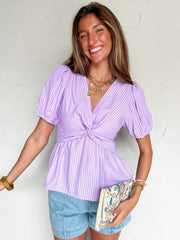 Woman wearing a light purple striped top and denim shorts against a white background