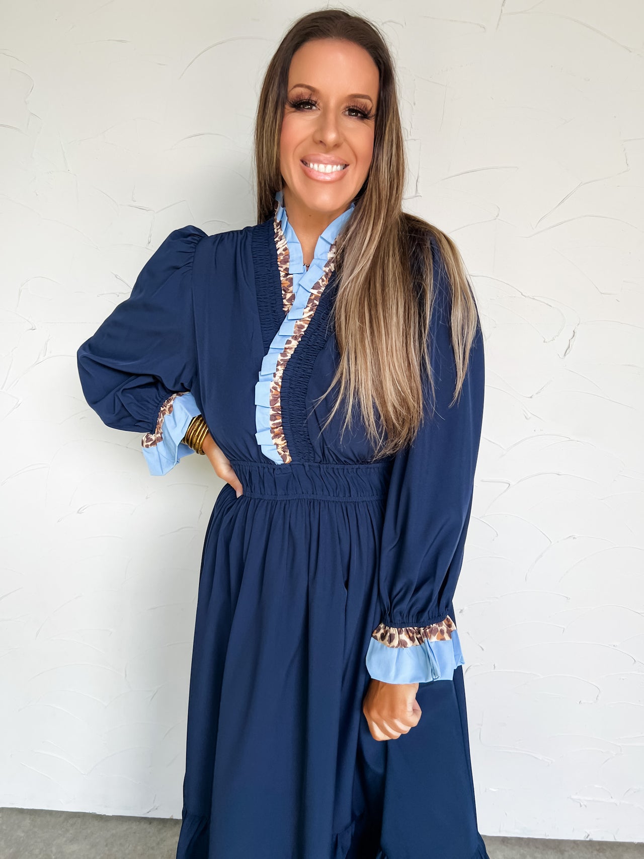 Woman wearing a blue dress with ruffled details against a white wall