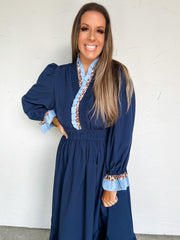 Woman wearing a blue dress with ruffled details against a white wall