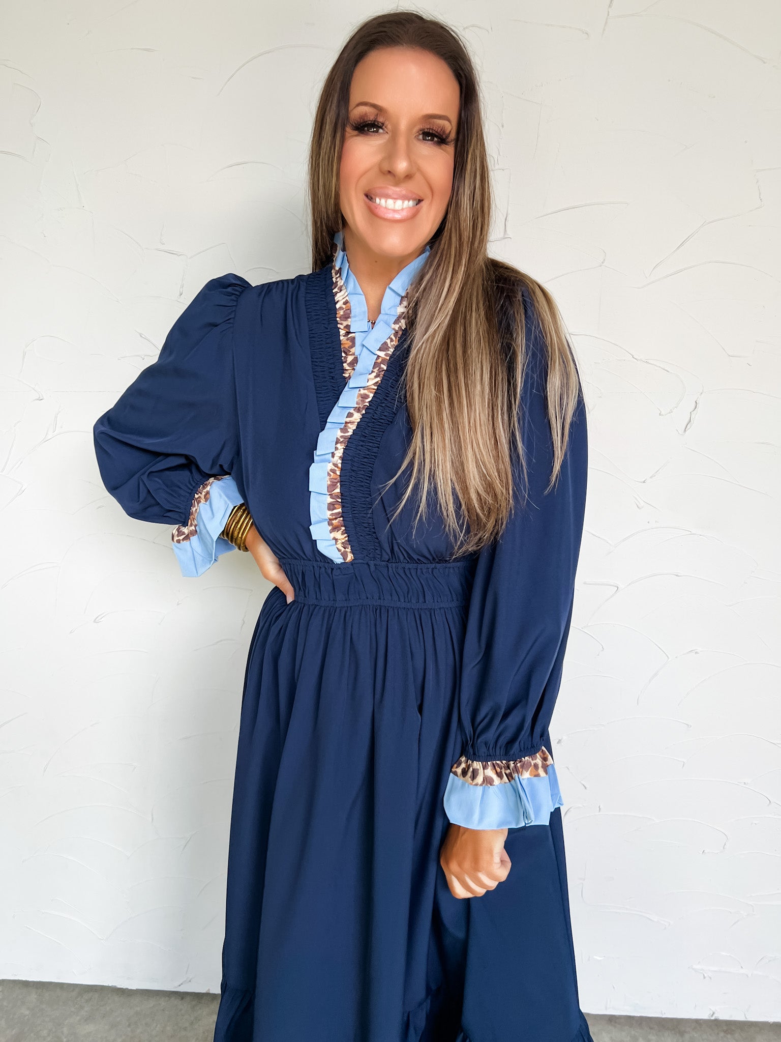 Woman wearing a blue dress with ruffled details against a white wall