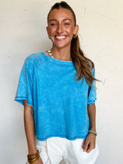 Woman wearing a blue acid washed cropped shirt and white shorts against a light background