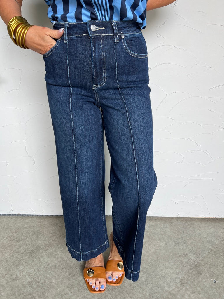 Person wearing dark blue jeans and a striped shirt against a white wall.