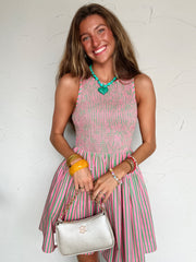 Woman wearing a pink and green striped dress holding a silver handbag against a white background