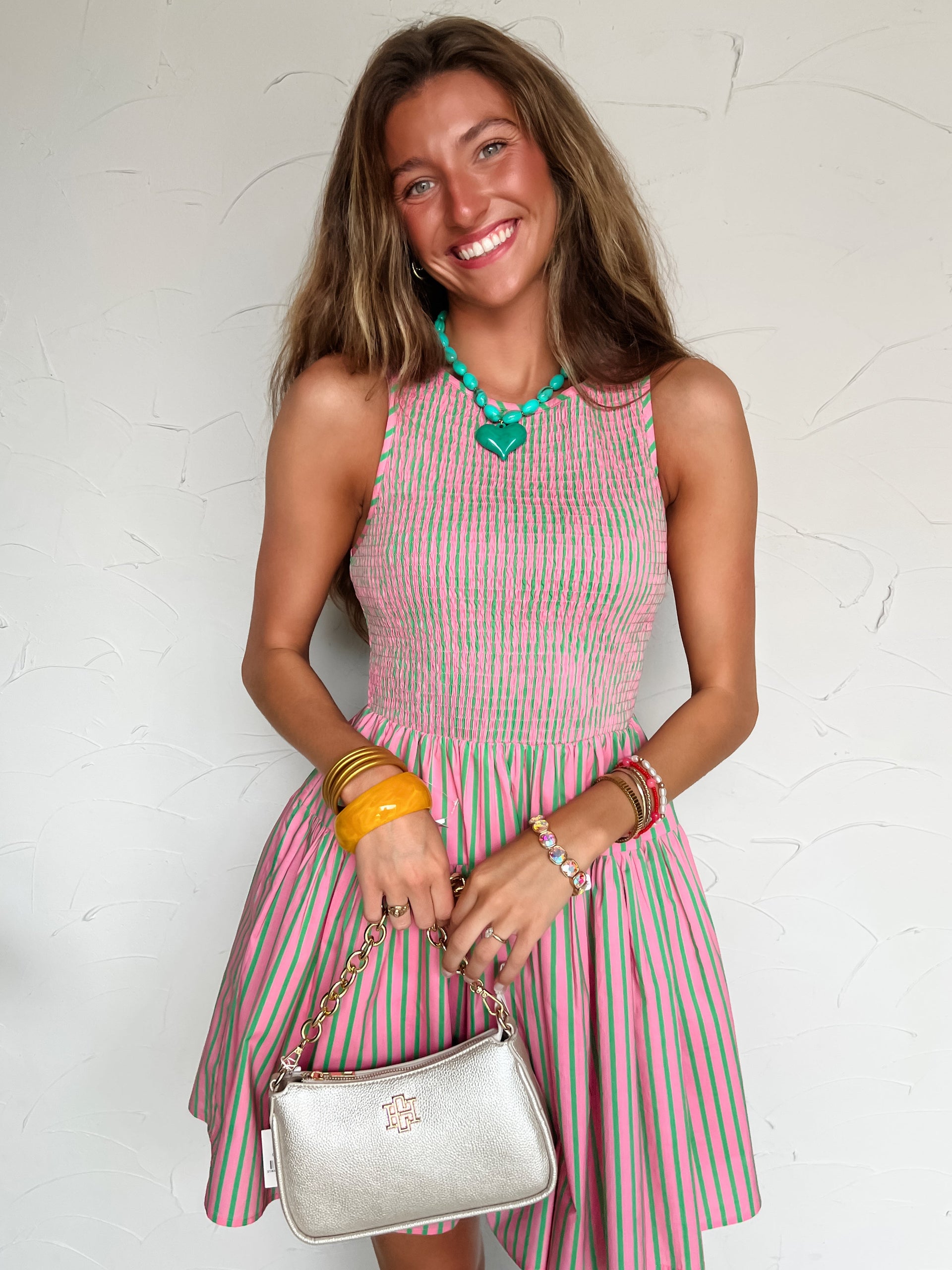 Woman wearing a pink and green striped dress holding a silver handbag against a white background