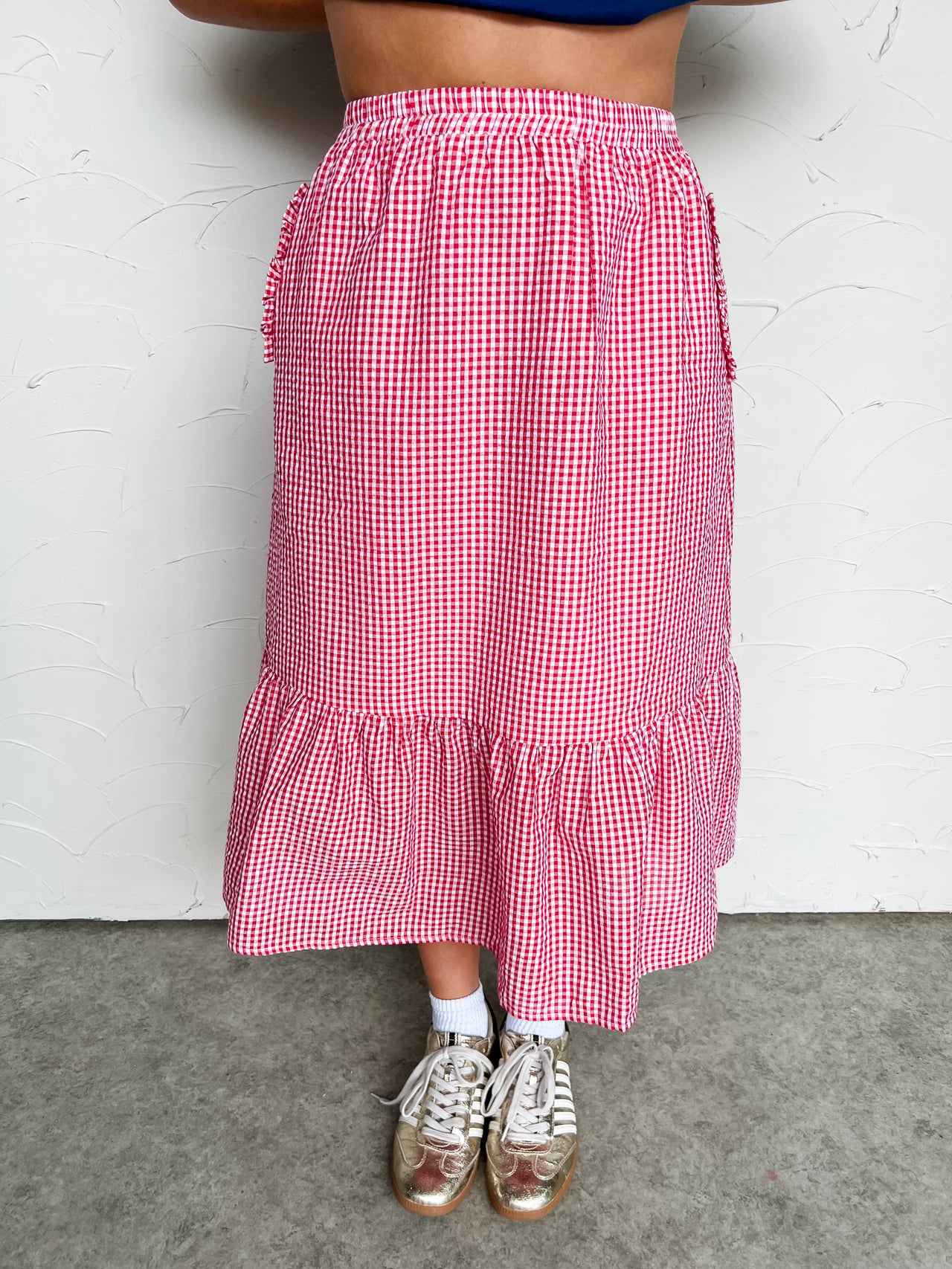 Person wearing a red and white checkered midi skirt with a plain background