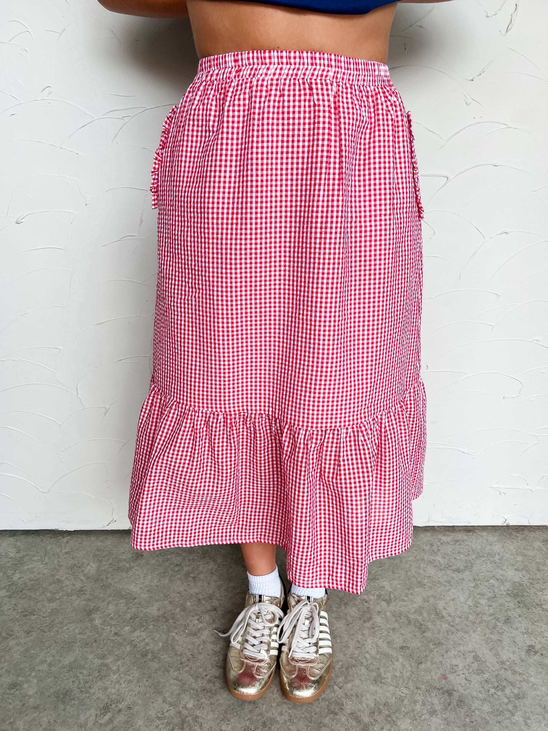 Person wearing a red and white checkered midi skirt with a plain background