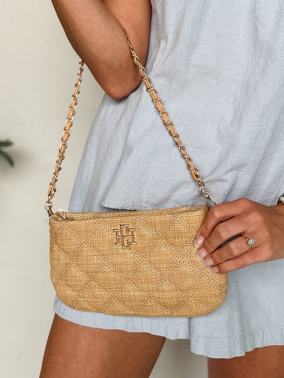 Person wearing a light blue dress holding a woven handbag with a blurred background