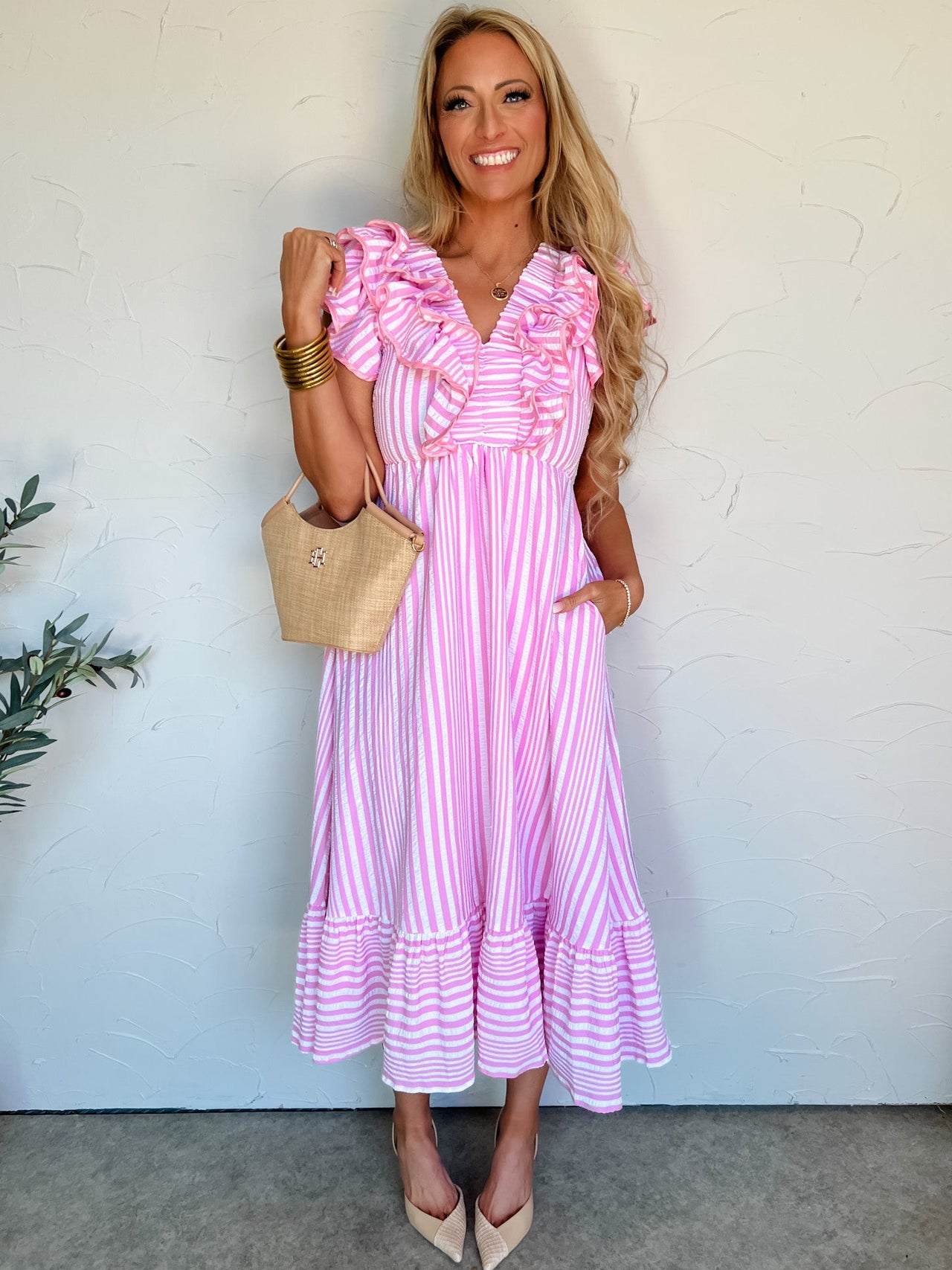 Woman wearing a pink and white striped dress with ruffled sleeves, standing against a white wall.