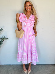 Woman wearing a pink and white striped dress with ruffled sleeves, standing against a white wall.