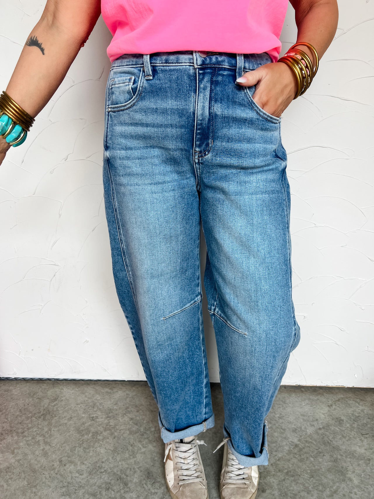 Person wearing blue jeans and a pink top against a white wall.