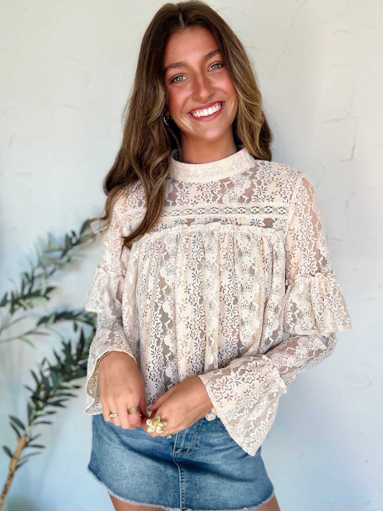 Woman wearing a lace top and denim skirt against a light blue wall.