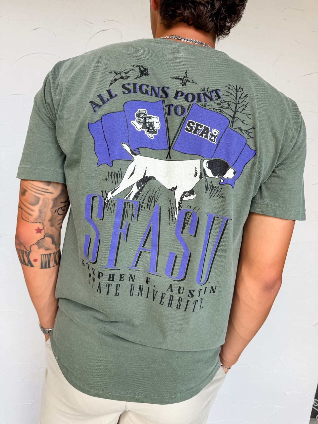 Person wearing a green t-shirt with a graphic design on the back, featuring text and a dog illustration.