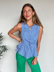 Woman wearing a blue and white checkered top and green pants against a white wall.