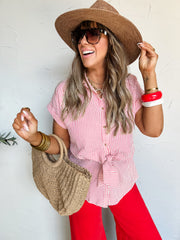 Woman wearing a red and white striped shirt, red pants, straw hat, and sunglasses, holding a woven bag against a light background.