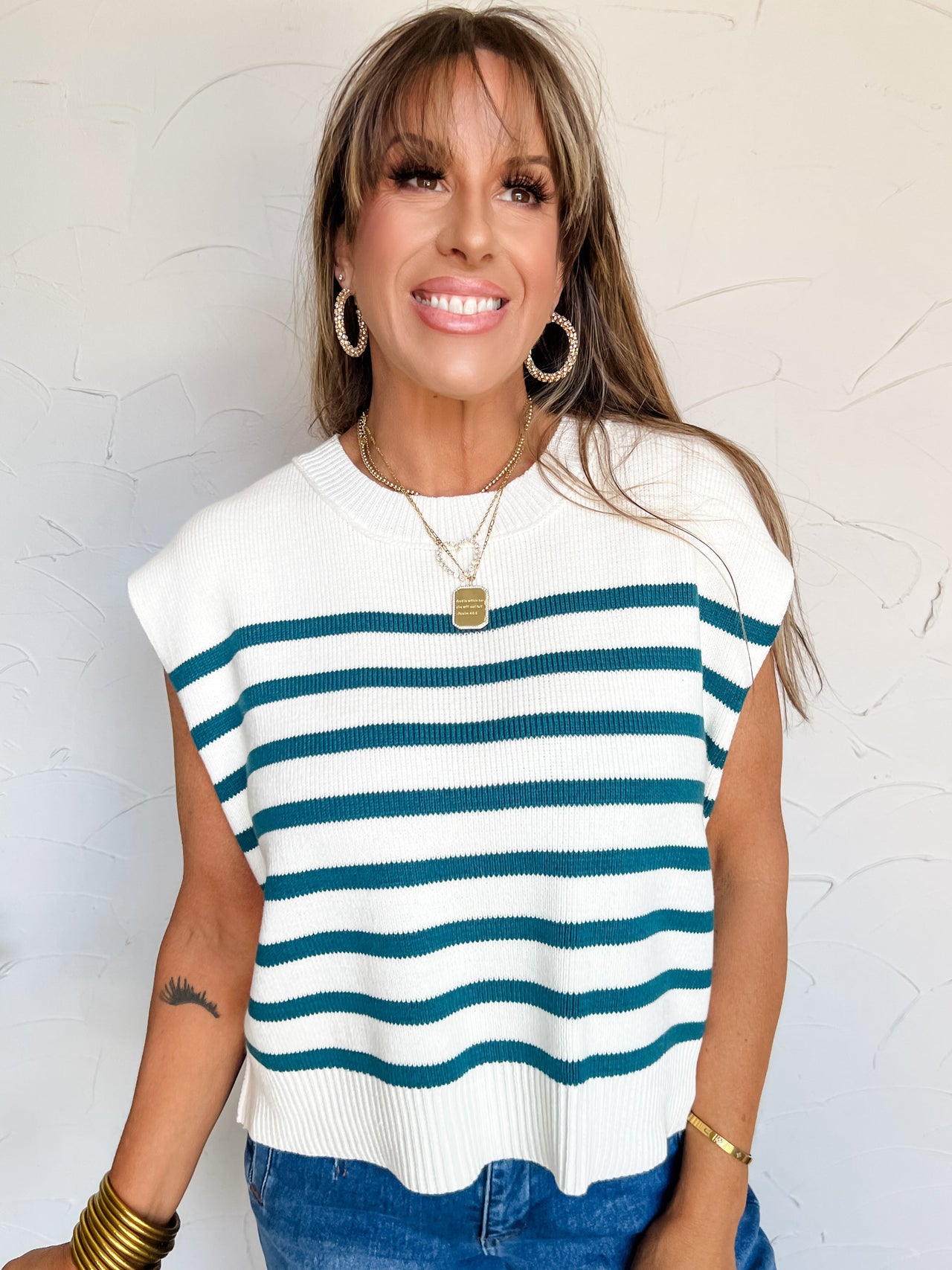 Woman wearing a white and teal striped sleeveless sweater against a light background