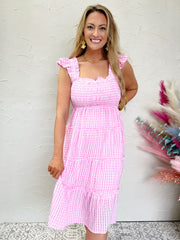 woman wearing a pink checkered dress in front of a white wall