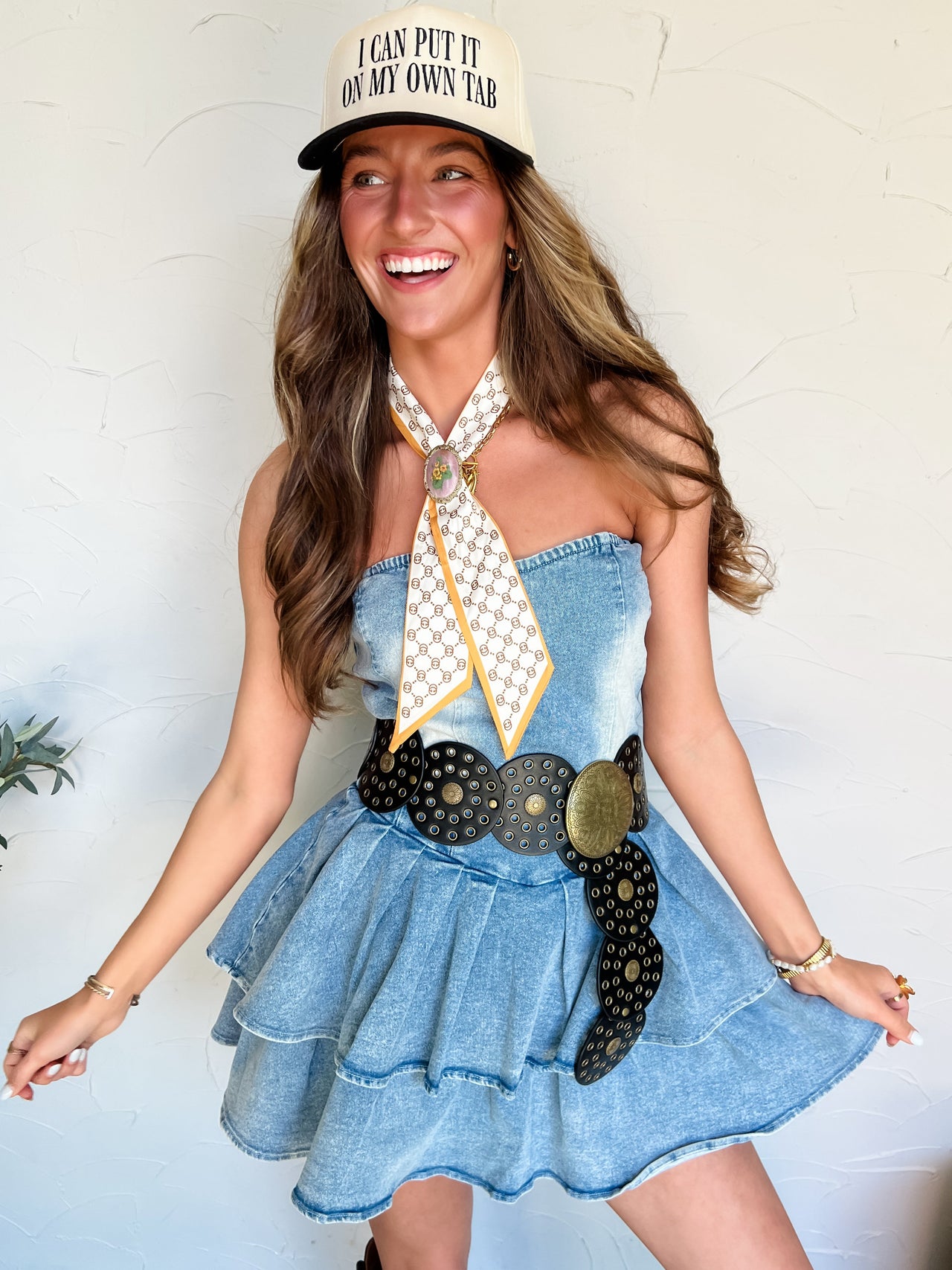 Woman wearing a denim dress, cap, and belt with a white background