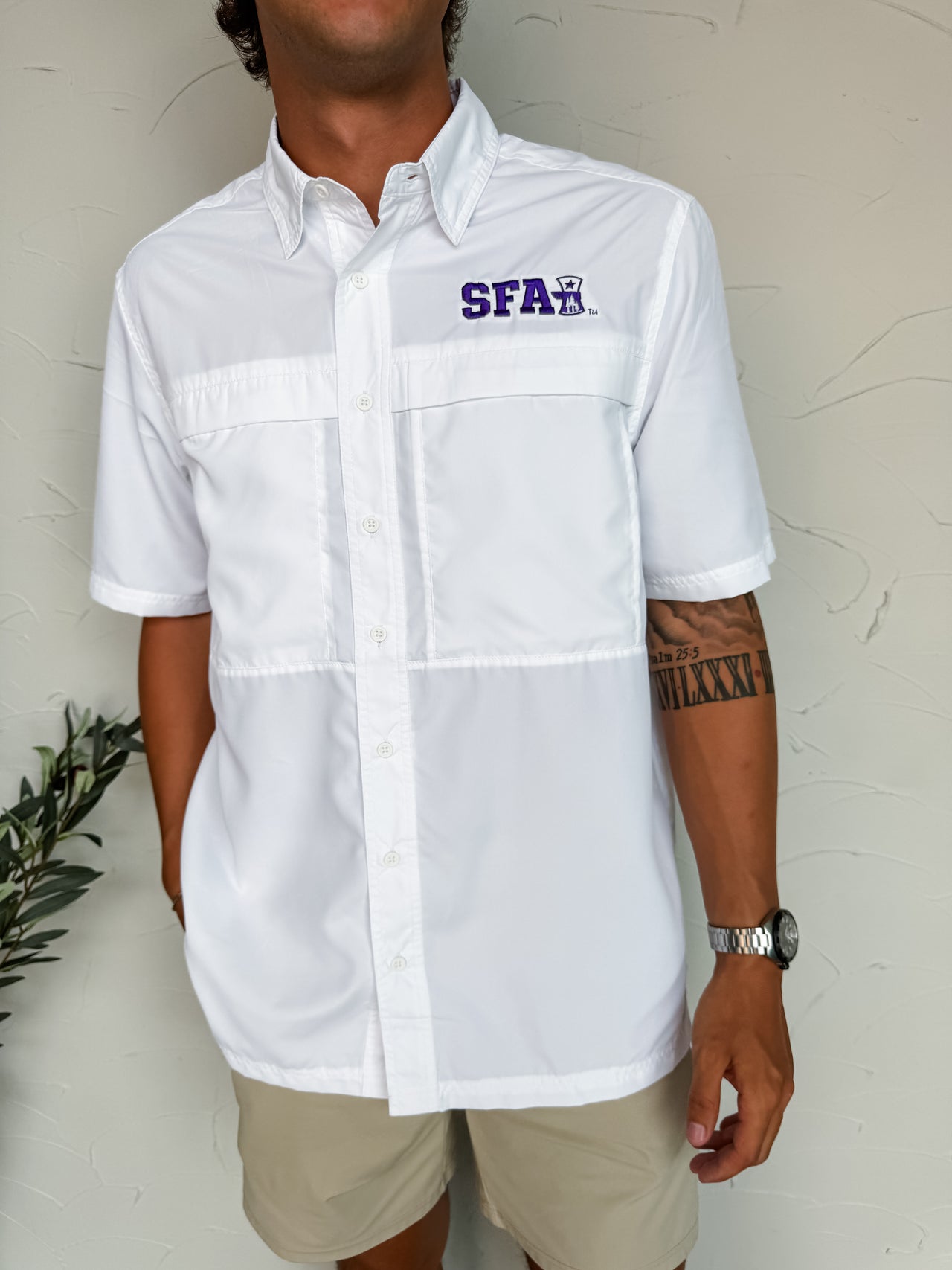 Person wearing a white button-up shirt with a logo on a light background