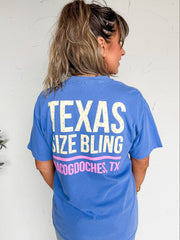 Person wearing a blue t-shirt with 'Texas Size Bling' text against a white wall.