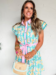 Woman wearing a colorful floral dress with a pink belt, holding a light blue handbag.