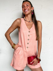 Woman wearing a pink linen romper with buttons against a white wall