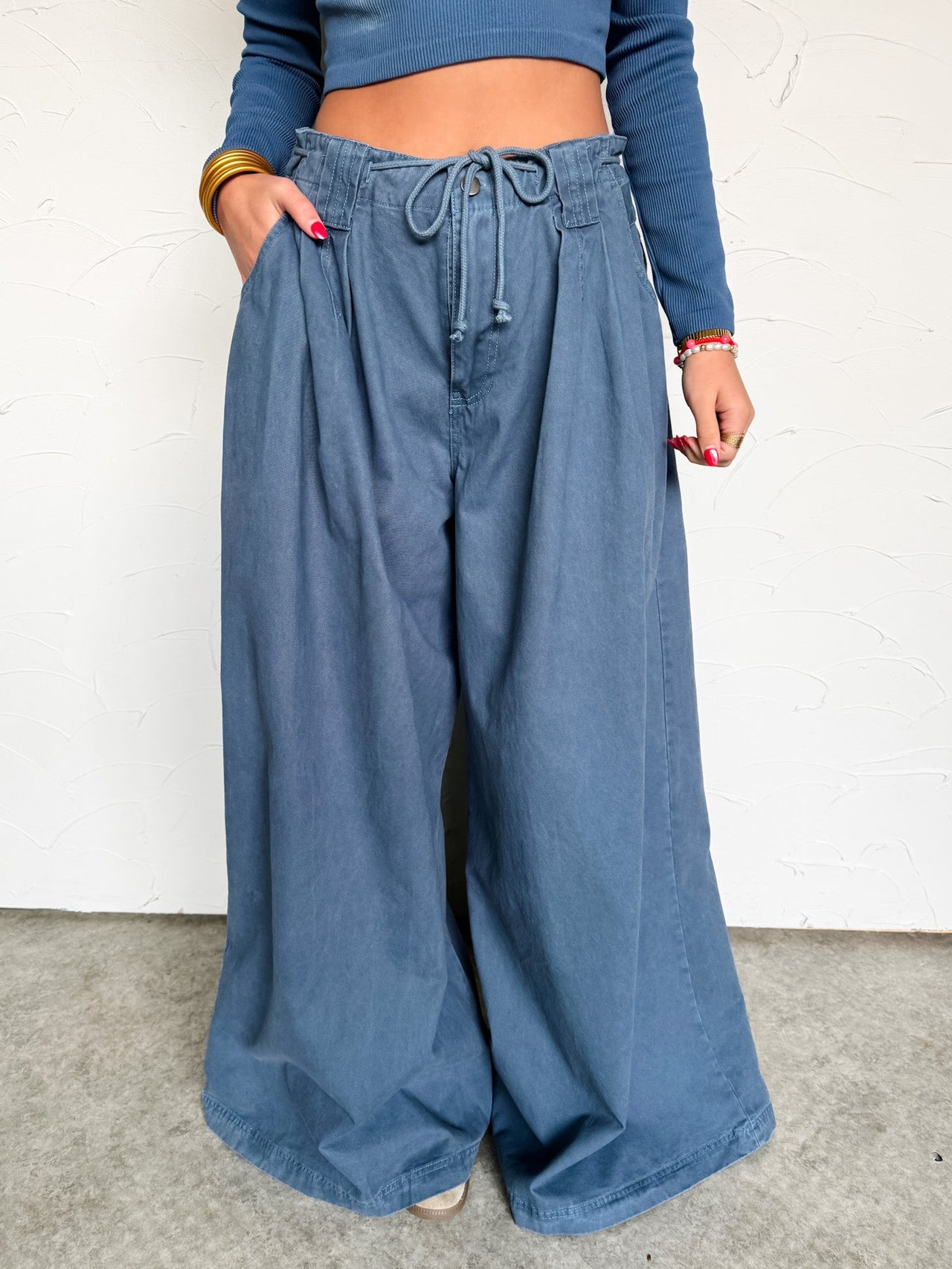 Person wearing blue wide-leg pants and a cropped blue top against a white wall.