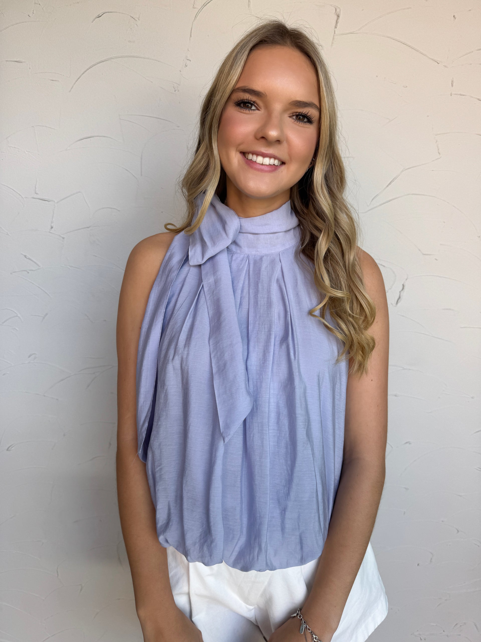 Woman wearing a light blue sleeveless top with a bow neckline against a white background