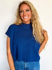 Woman wearing a navy blue sweater top and jeans against a white background