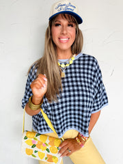 Woman wearing a navy checkered knit top and yellow pants with a floral bag, against a white background