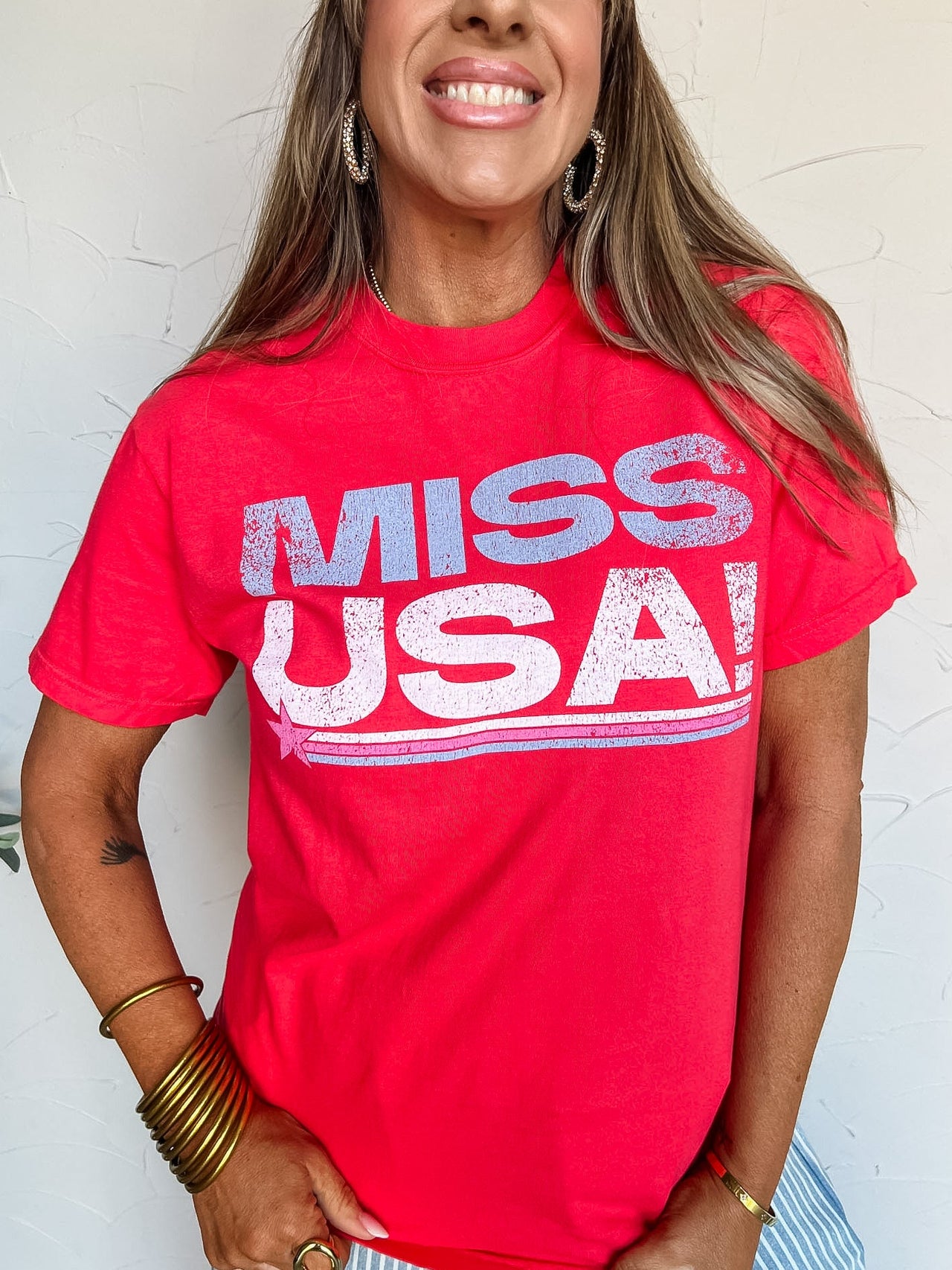 Woman wearing a red 'Miss USA' t-shirt against a white wall
