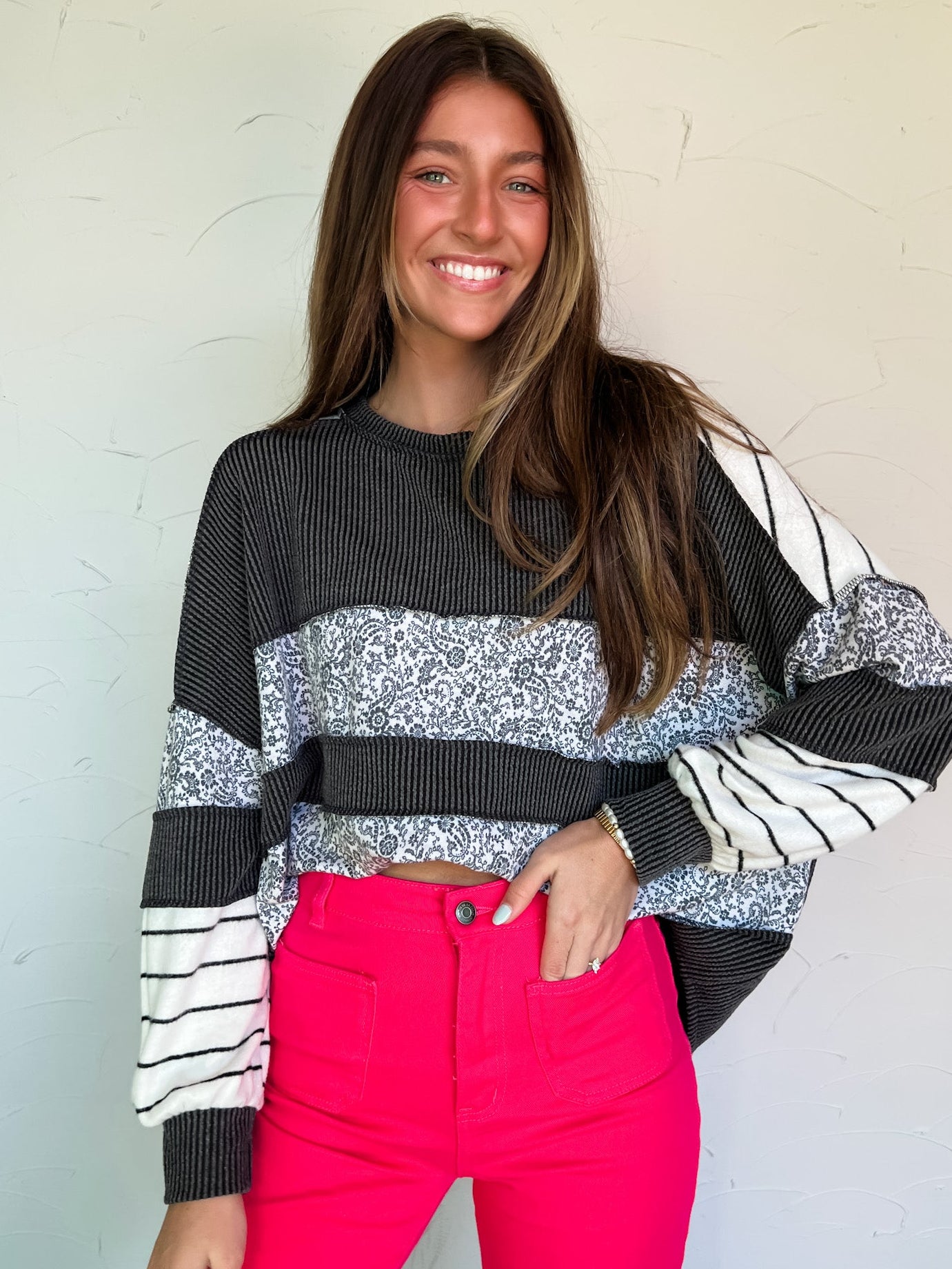 Woman wearing a black, white, and gray patterned sweater with pink pants against a light background