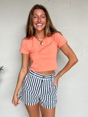 Woman wearing a coral top and striped shorts against a white textured wall