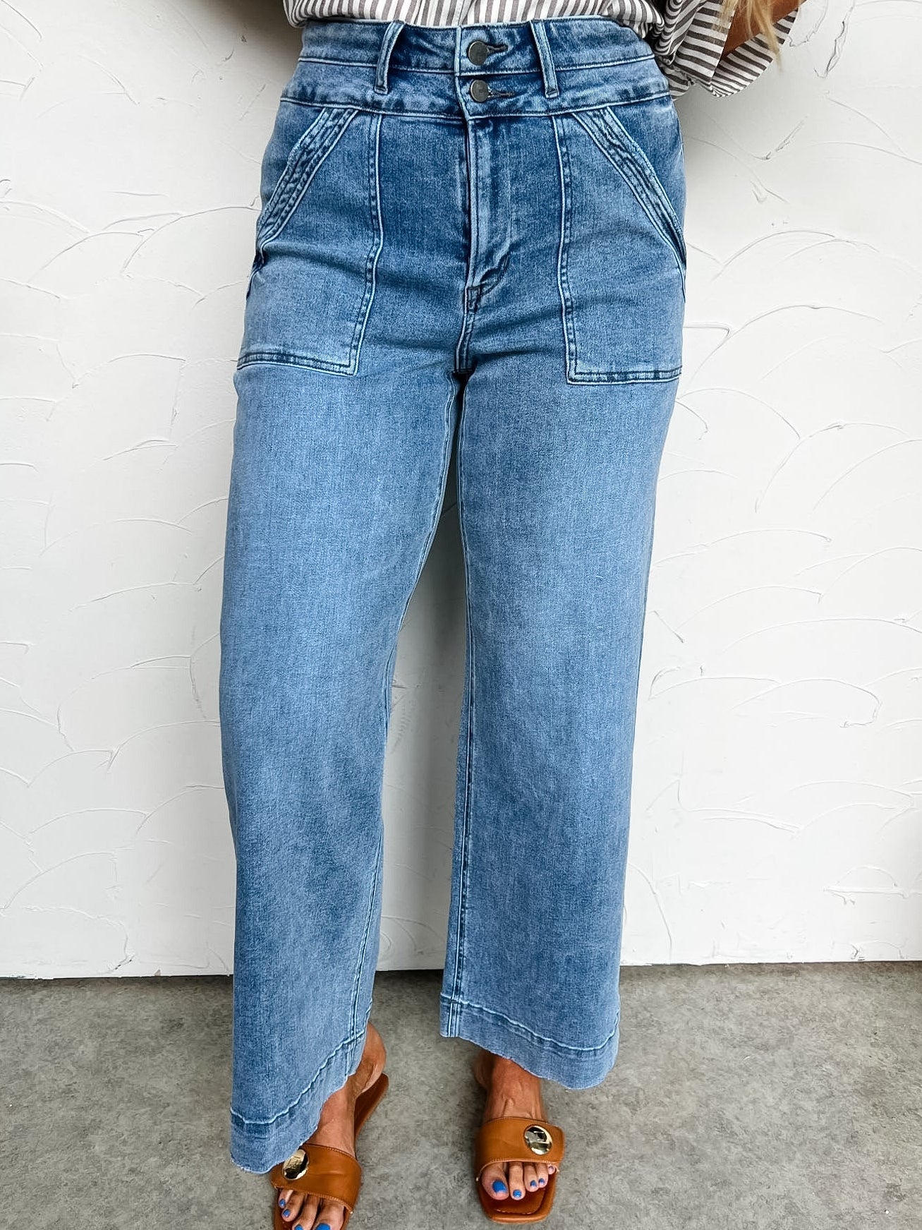 Person wearing blue jeans and a striped shirt against a white wall.
