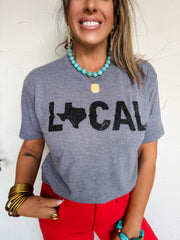 Woman wearing a gray t-shirt with 'LOCAL' and a map of Texas design, smiling against a white background.