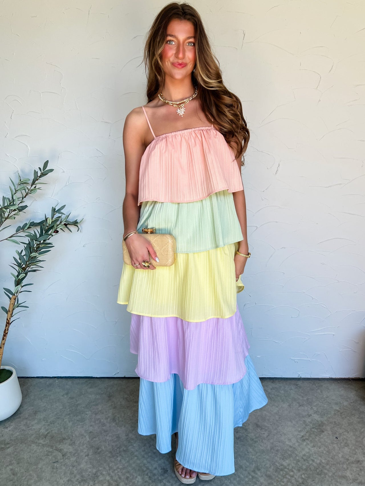 Woman wearing a pastel tiered dress with a white wall and plant in the background