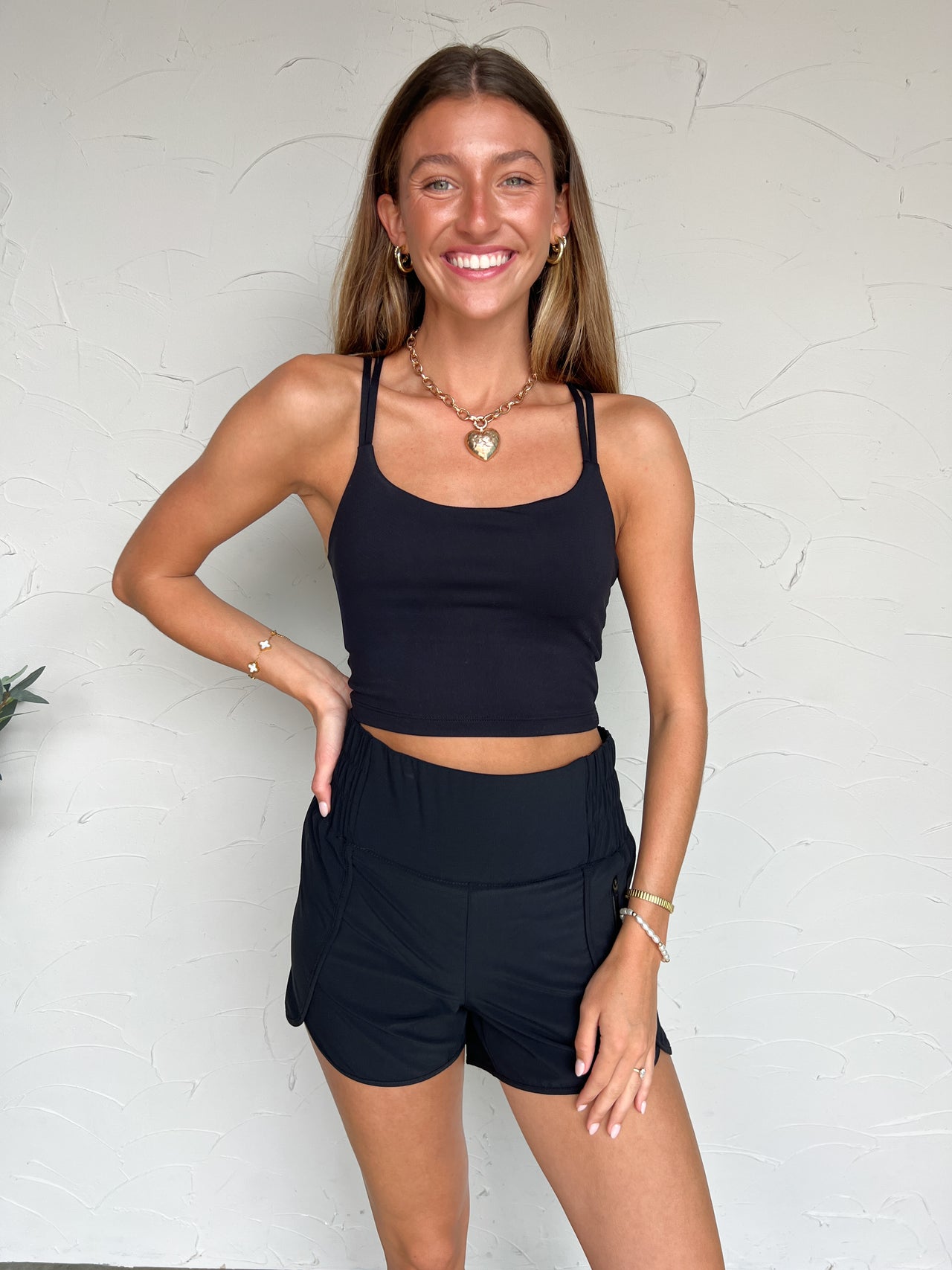 Girl in black tank top and black shorts in front of plain wall 